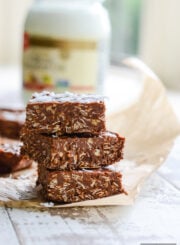 Three chocolate peanut butter coconut bars stacked on top of each other with a sheet of parchment paper underneath the stack
