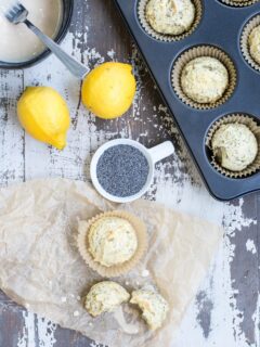 Overhead shot of a table with a muffin tin, lemons, glaze, and other items. Two muffins are nearby on the counter.
